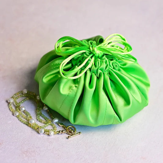 Green drawstring bag with a necklace on a light gray background