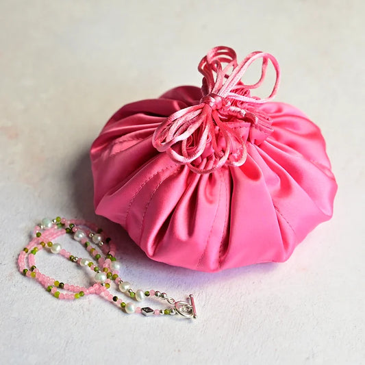 Pink drawstring bag with a necklace on a light background