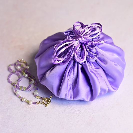 Purple satin drawstring bag with a necklace on a light background