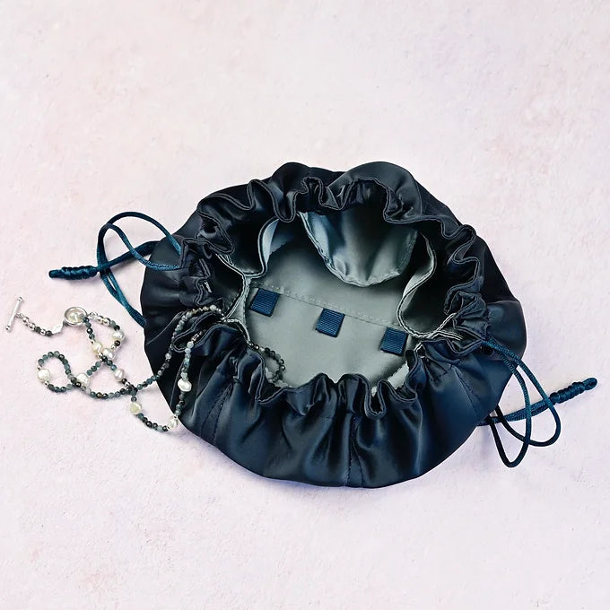 Dark blue drawstring bag with jewellery on a light pink background