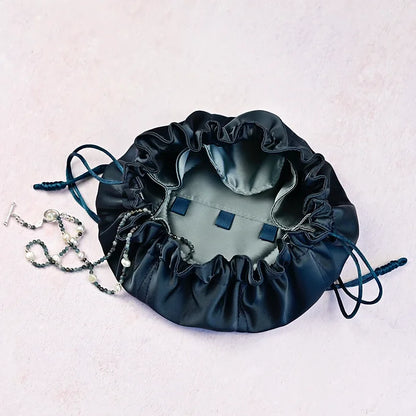 Dark blue drawstring bag with jewellery on a light pink background