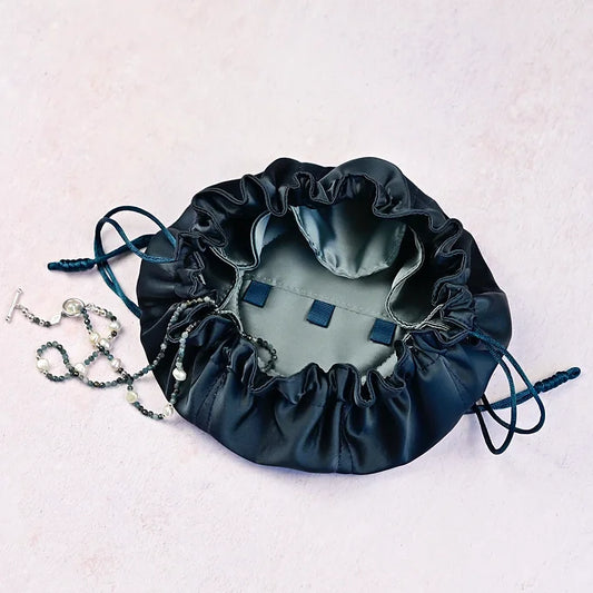 Dark blue drawstring bag with jewellery on a light pink background