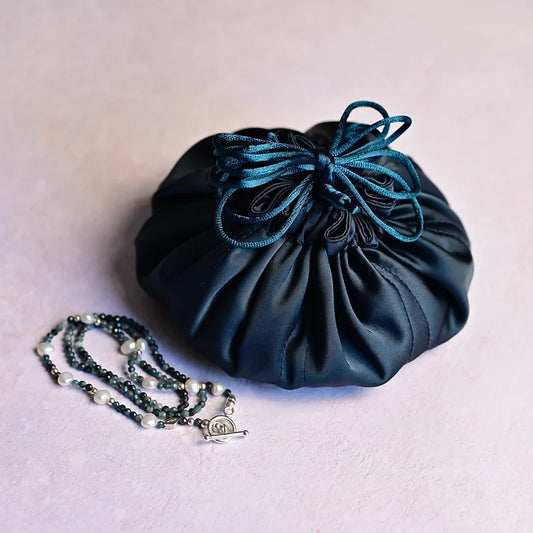 Blue drawstring pouch with a necklace on a light pink background