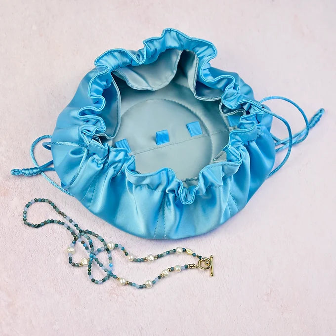 Blue drawstring bag with jewelry on a light pink background