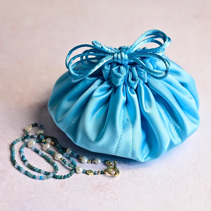Blue satin drawstring bag with a blue beaded necklace on a light background