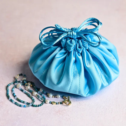 Blue satin drawstring bag with a blue beaded necklace on a light background
