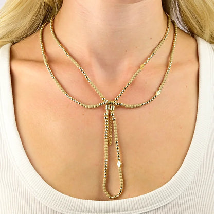 Gold beaded necklace worn by a person on a plain background