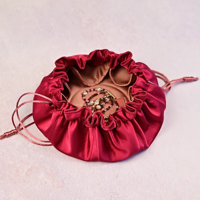 Red satin jewelry pouch with a gold and pearl necklace on a light pink background