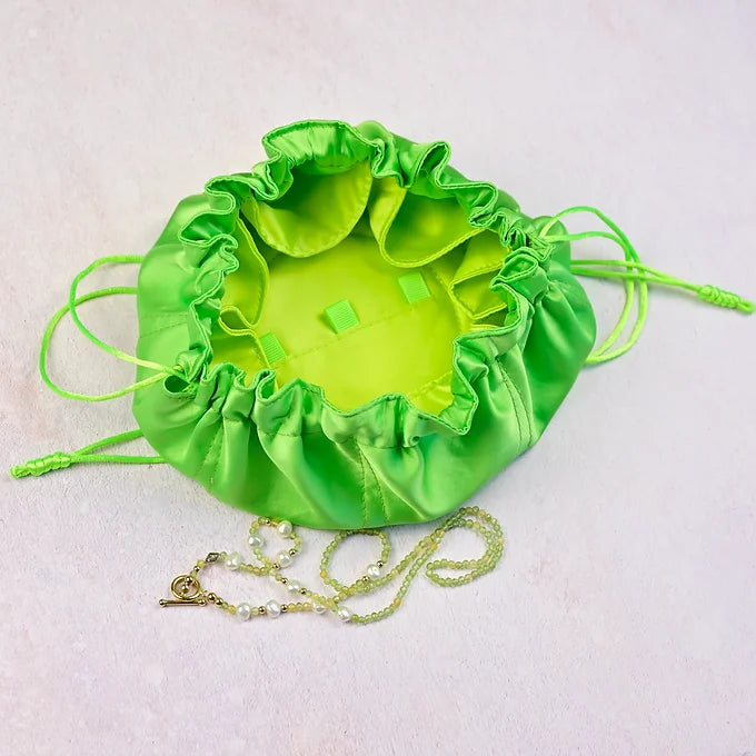 Green satin drawstring bag with a necklace on a light pink background