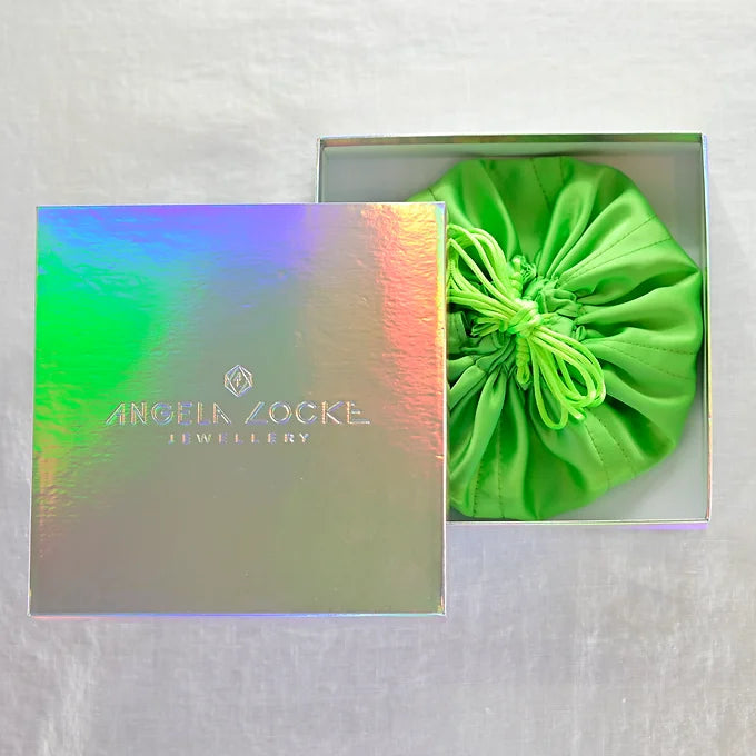 Green drawstring bag inside a box with 'Angela Zocke Jewellery' branding on a light gray background