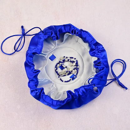 Blue satin jewelry bag with a white interior containing jewelry on a light gray background