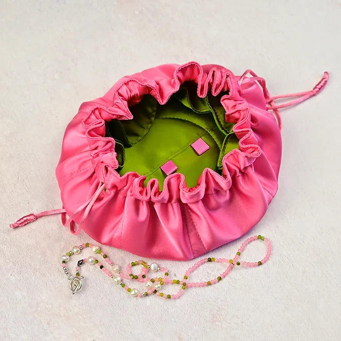 Pink drawstring bag with green interior, containing small pink loops and a necklace on a light beige background.