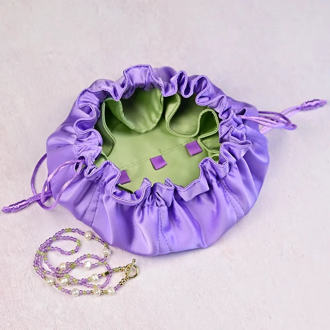 Purple drawstring bag with green interior holding small purple loops a light gray background.
