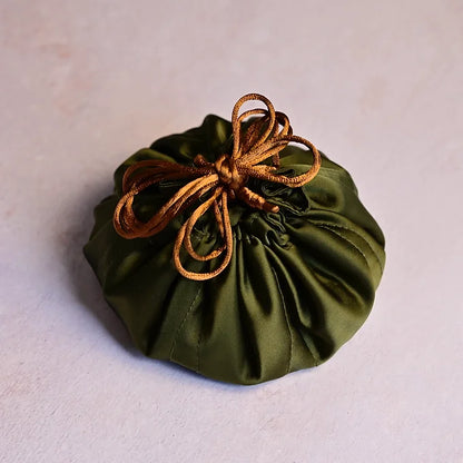 Green fabric pouch with a brown drawstring on a light gray background