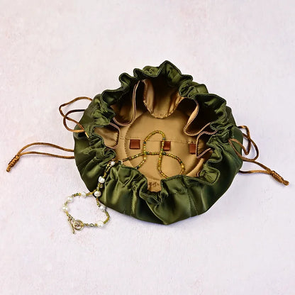 Green drawstring pouch with jewelry on a light pink background