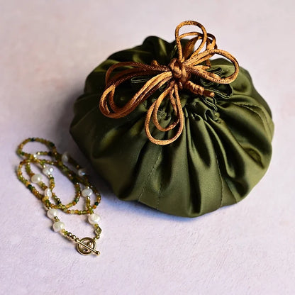 Green drawstring bag with a necklace on a light purple background